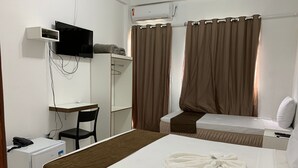 Una habitación de hotel con una cama, un escritorio, una silla, un televisor y un aire acondicionado.