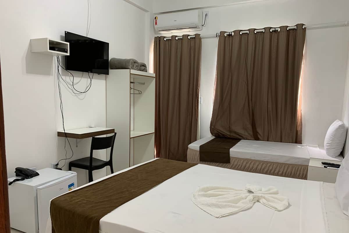 Una habitación de hotel con una cama, un escritorio, una silla, un televisor y un aire acondicionado.