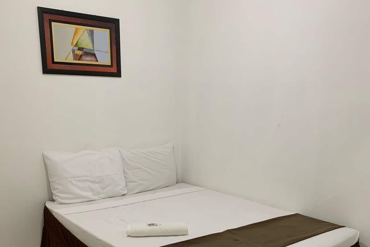 Una cama individual con una colcha marrón y ropa de cama blanca, un almohadón blanco y un cuadro en la pared.