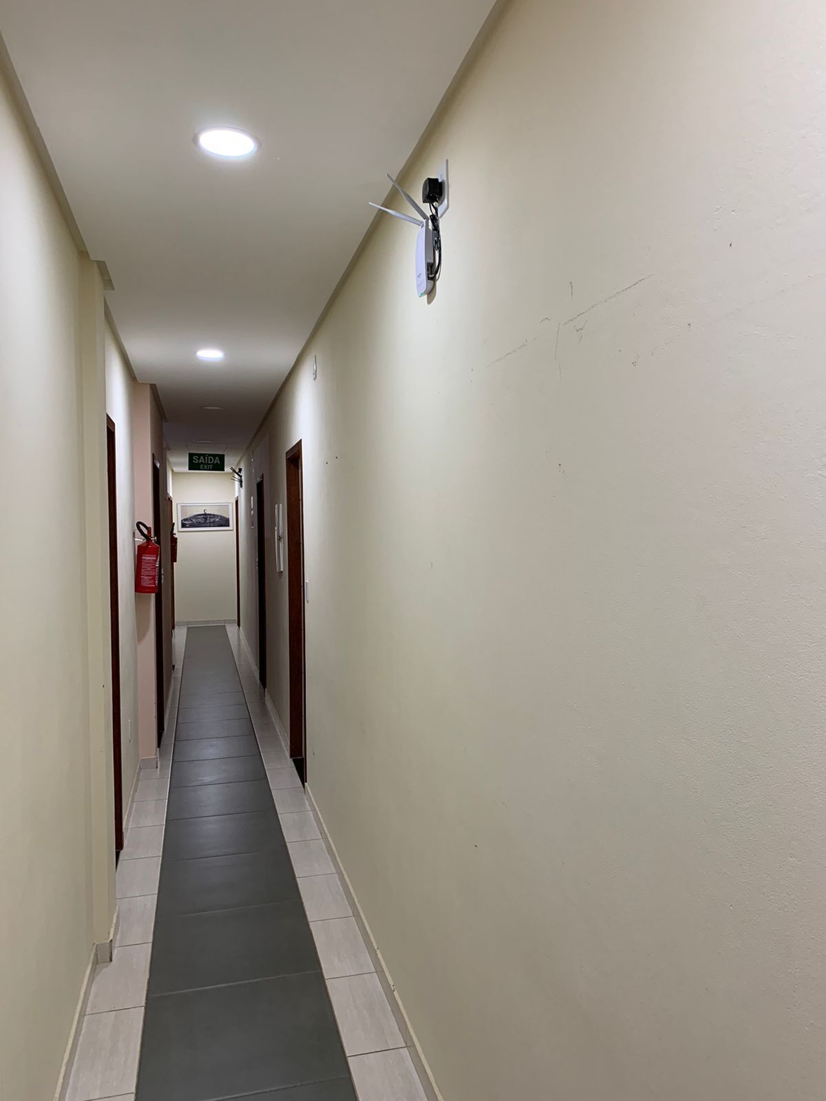 A long, narrow hallway with a tiled floor, a fire extinguisher on the left, and a sign indicating an exit.