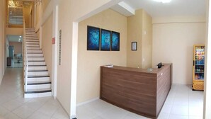 Zona de recepción de hotel con mostrador de madera, una escalera y una máquina expendedora.