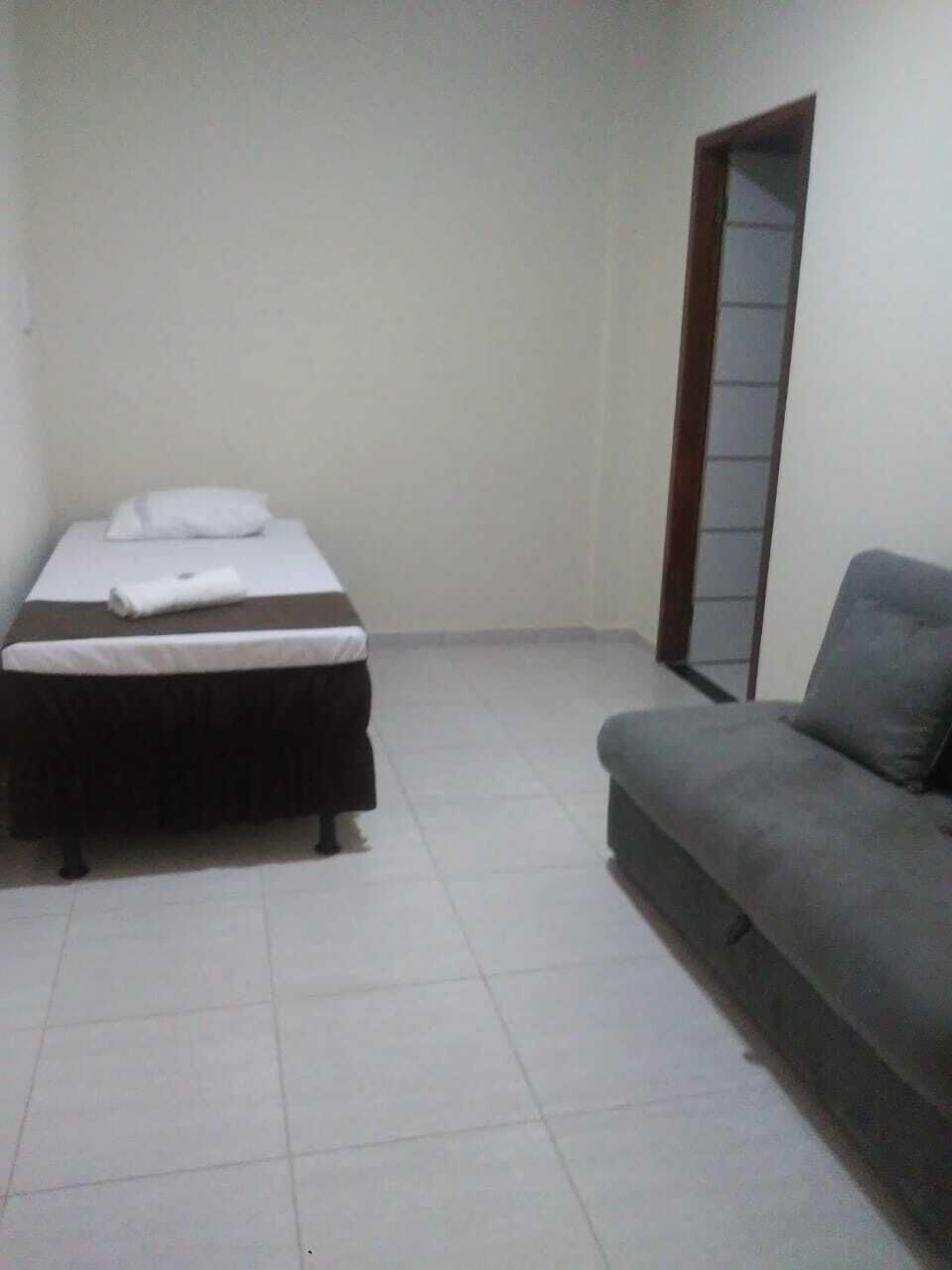 Habitació petita i poc moblada amb un llit, un sofà i una porta que dona a una altra habitació.