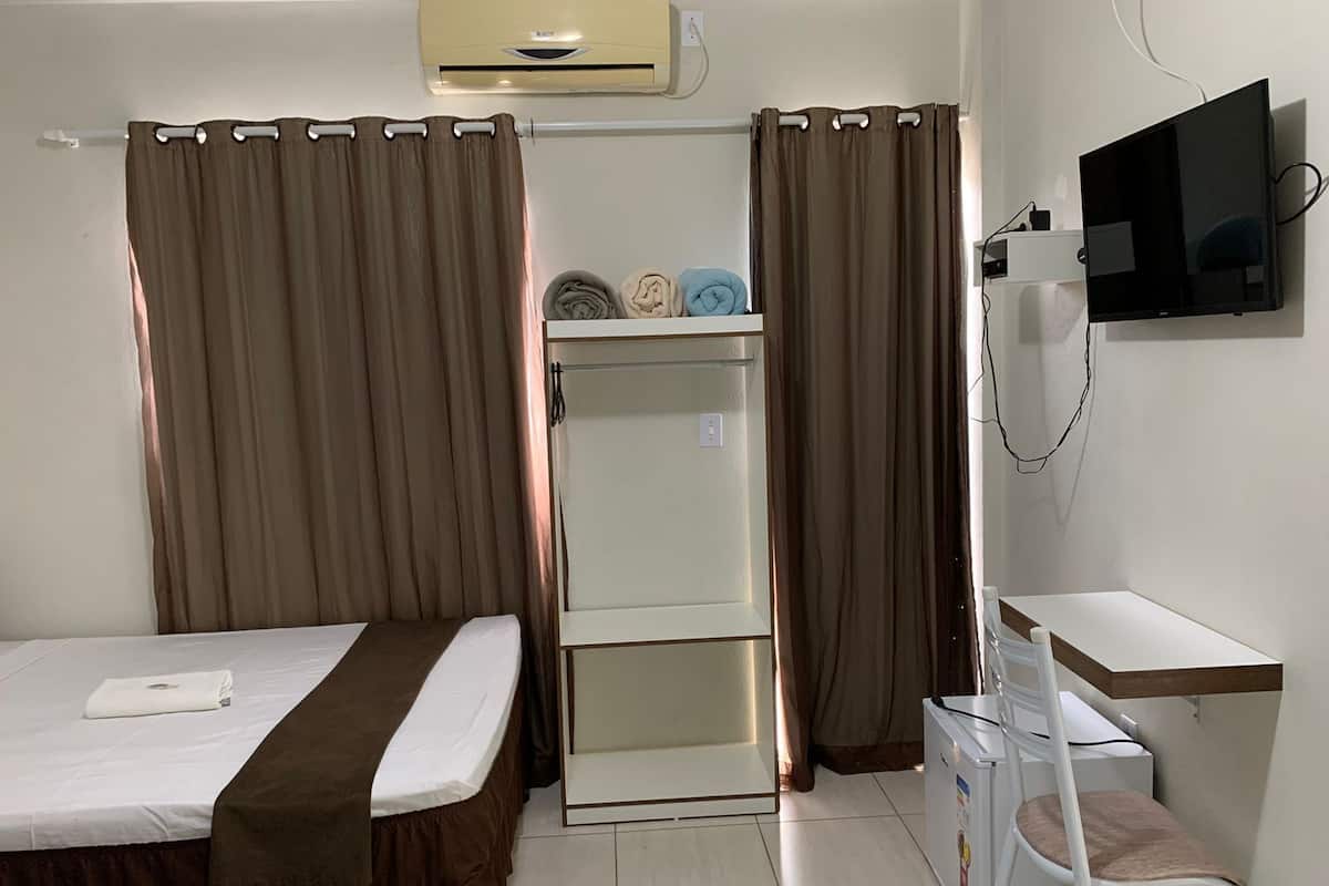 Una habitación de hotel con cama, escritorio, silla, televisor y armario.