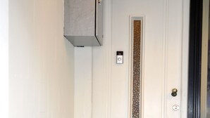 A white door with a vertical strip of decorative glass, a doorbell, and a mail slot. - Zaras Studio Apollo (Zandvoort)