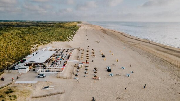 An aerial view of a beach with a large building, likely a hotel, featuring outdoor seating and umbrellas. - Zaras Studio Apollo (Zandvoort)