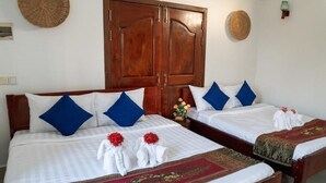 Une chambre d’hôtel avec deux lits, chacun agrémenté de draps blancs, d’oreillers bleus et d’un tapis décoratif rouge. On y trouve également des armoires en bois et un climatiseur fixé au mur.