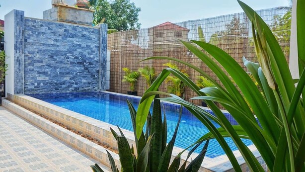 Une piscine aux murs en pierre, avec une clôture en bambou en arrière-plan.