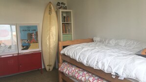 Ett sovrum med en våningssäng, en surfbräda som står lutad mot väggen, en bokhylla och en affisch på väggen.