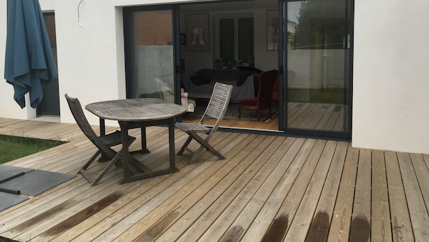 En modern uteplats med ett trädäck, ett bord och två stolar.