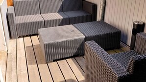 Un espace extérieur aménagé, abrité et doté de meubles en osier et d’une terrasse en bois.
