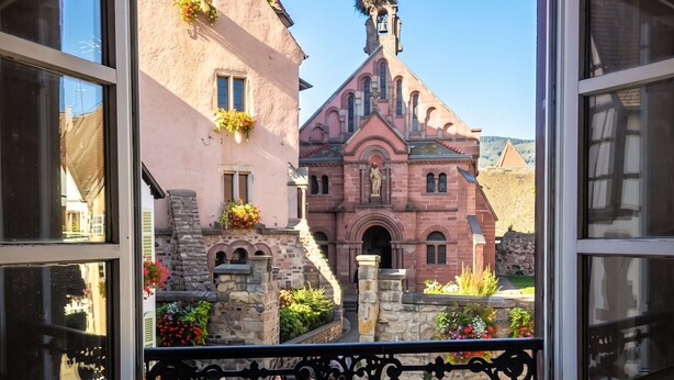 Une vue à travers la fenêtre d’un bâtiment doté d’un clocher et de jardinières fleuries.