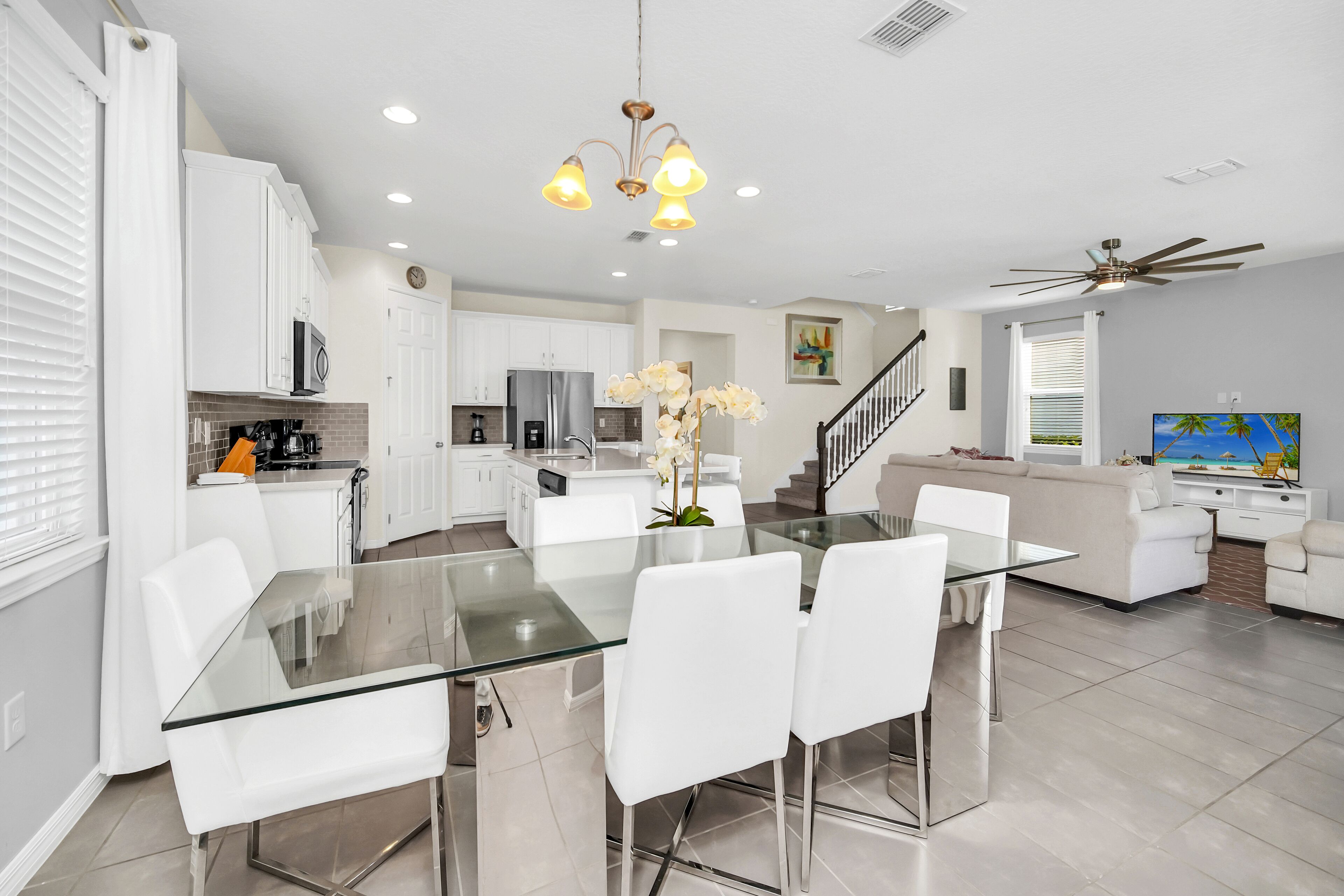A modern kitchen with white cabinets, a glass dining table, and white chairs.