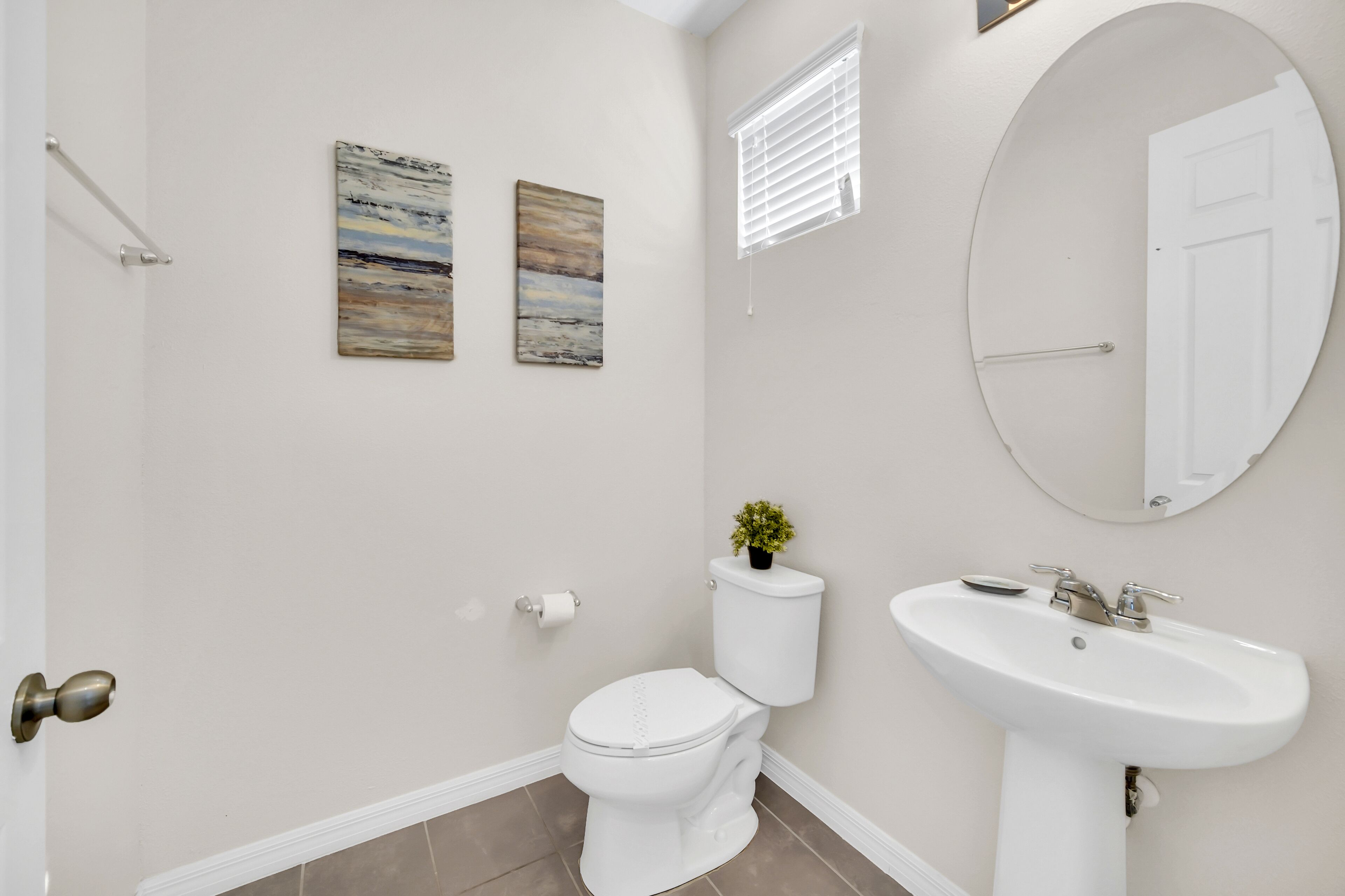 A bathroom with a toilet, sink, and two wall-mounted paintings.
