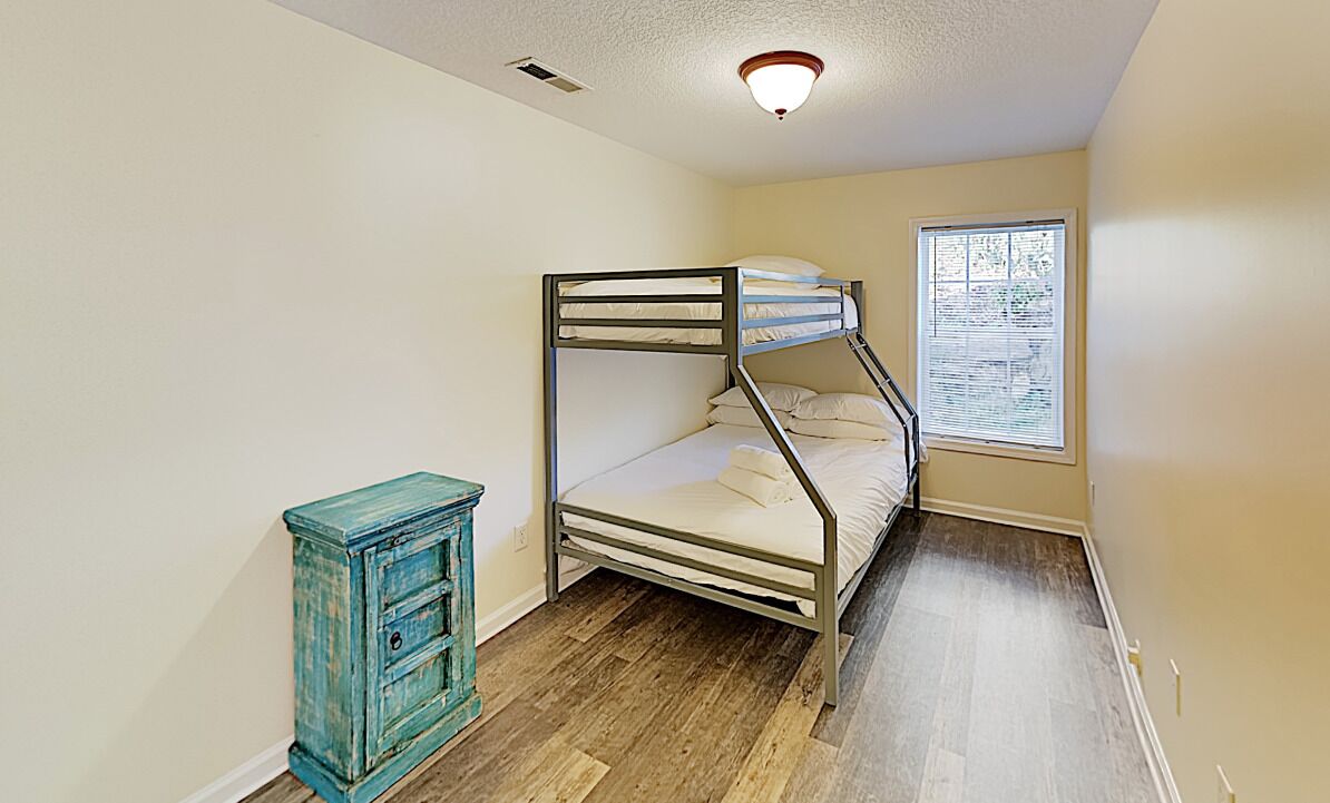 A small, single-bedded room with a bunk bed, a small wooden cabinet, and a window with blinds.