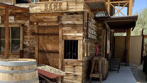 A rustic wooden building with a wooden barrel, a wheelbarrow, and a wooden table. - LAZY C RANCH - POOL, ANIMALS, DESERT RANCH EXPERIENCE (Palm Springs)