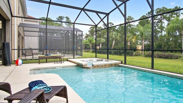 Una piscina con jacuzzi, rodeada por una estructura de vidrio y mobiliario exterior.