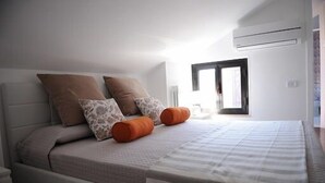 Un lit bien fait, avec une couvre-lit à rayures et deux oreillers, une table de chevet avec une lampe, et une fenêtre donnant sur l’extérieur.