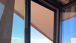 Un balcón con mobiliario de mimbre, una planta en maceta y vistas al mar.
