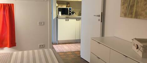 A bedroom with a bed, a dresser, and a view into the kitchen.