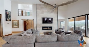 A modern living room with a sectional sofa, a fireplace, a flat-screen TV, and a balcony with a view.