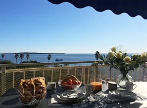 Une table dressée avec des aliments pour le petit-déjeuner, un vase rempli de fleurs et une vue sur la mer.