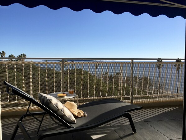 Relax on a comfortable lounger with a pillow and enjoy the view of the body of water and distant hills from the outdoor deck.