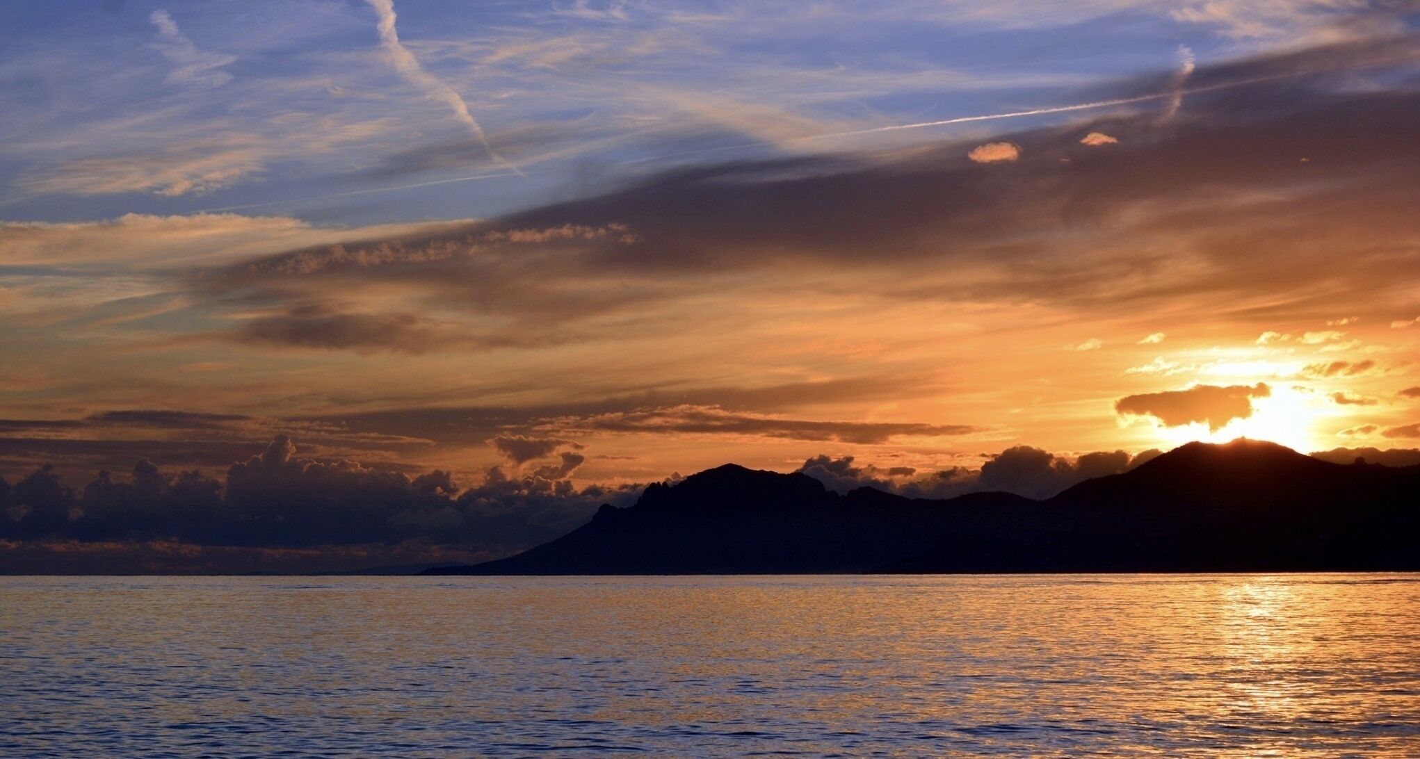 Tramonto sul mare calmo, con montagne sullo sfondo.