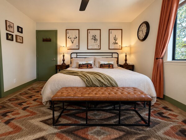 A bedroom with a bed, two bedside tables, a bench, a clock, and framed pictures on the wall.