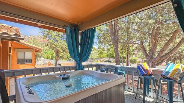 Un jacuzzi en una terraza de madera con vista a árboles y un edificio al fondo.