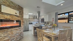 Una cocina moderna con pared de piedra, chimenea empotrada y comedor con sillas de madera y una mesa dispuesta para cuatro.