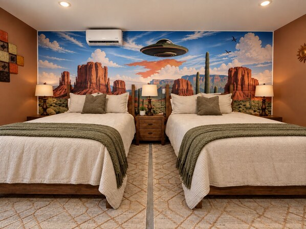 Habitación con espejo, dos camas, un mural de paisaje desértico y una lámpara en el techo.