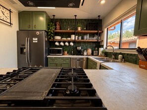 Une cuisine moderne équipée d’une cuisinière à gaz, d’appareils électroménagers en acier inoxydable et d’une fenêtre donnant sur l’extérieur.