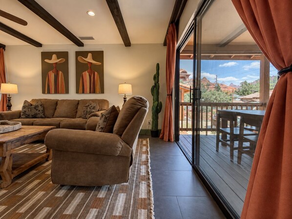 Una sala de estar con un sofá modular, dos lámparas, un cactus y vistas a un paisaje montañoso a través de amplios ventanales.