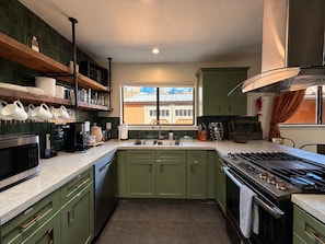 Una cocina con gabinetes verdes, un lavamanos de acero inoxidable y una estufa a gas.