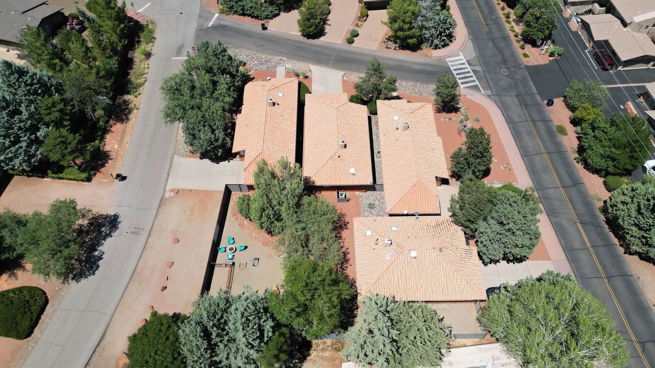 An aerial view of a residential area with three houses, each with a tiled roof and surrounded by trees.