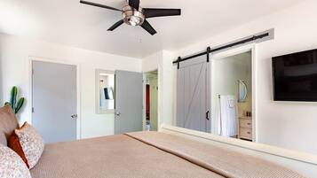 A bedroom with a bed, a ceiling fan, a sliding door, and a television mounted on the wall.