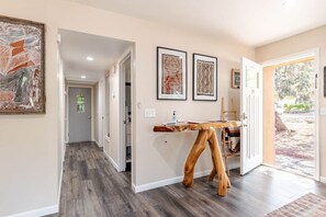 A hallway with a wooden table and chairs, framed artwork on the walls, and a door leading outside. - Iconic Sedona House | Walk to Uptown + Hot Tub, The Sedona House ~ Red Rock Getaway (Sedona)