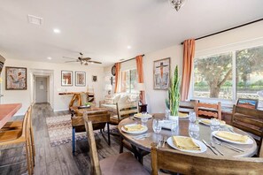 A dining area with a round table set for four, wooden chairs, and a view of the outdoors through large windows. - Iconic Sedona House | Walk to Uptown + Hot Tub, The Sedona House ~ Red Rock Getaway (Sedona)