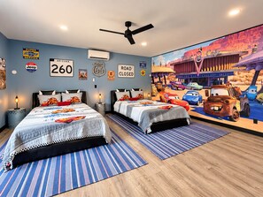 Ein Schlafzimmer mit zwei Betten, einem Deckenventilator und einem Wandgemälde mit animierten Autos.