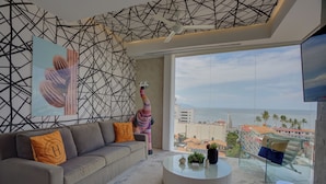 Uma sala de estar moderna com um sofá, uma mesa de centro de vidro e uma janela grande com vista para a cidade.