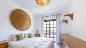 Ein ordentlich eingerichtetes Schlafzimmer mit Bett, Nachttischen, einer Pendelleuchte und einem Fenster mit Vorhängen.