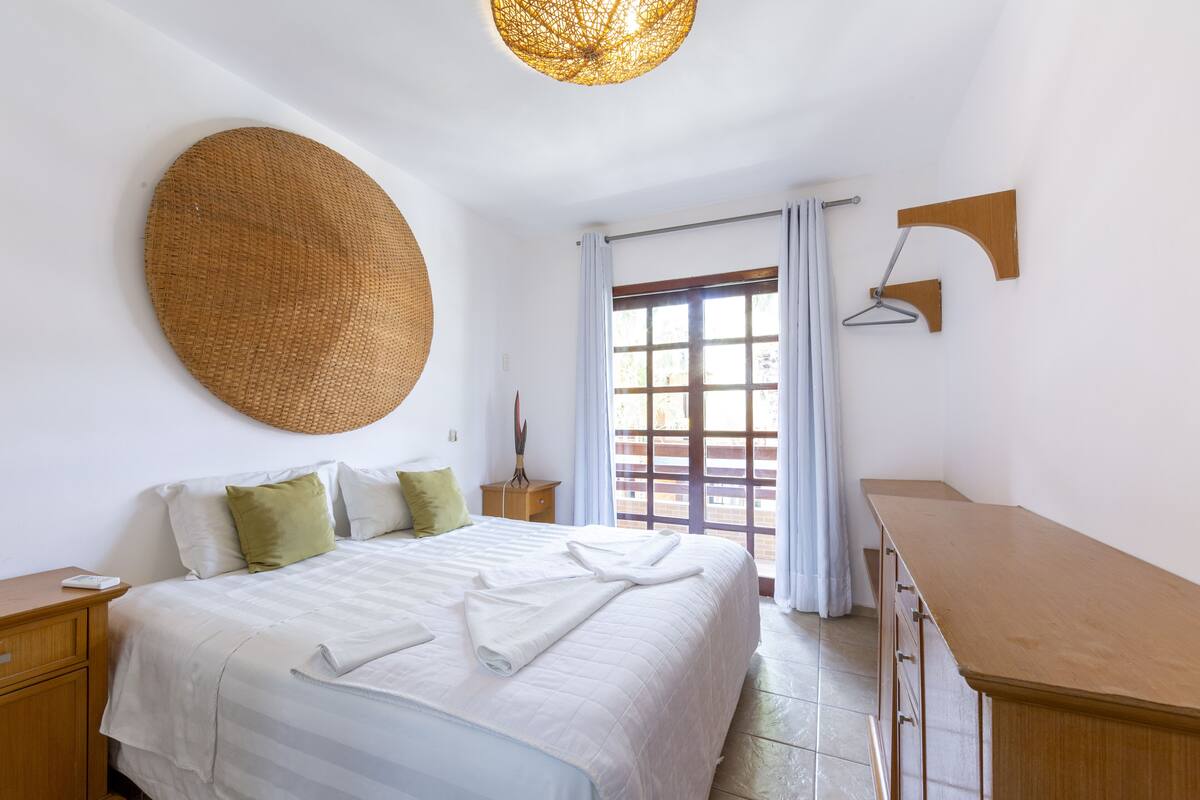 A neatly arranged bedroom with a bed, bedside tables, a hanging light fixture, and a window with curtains.