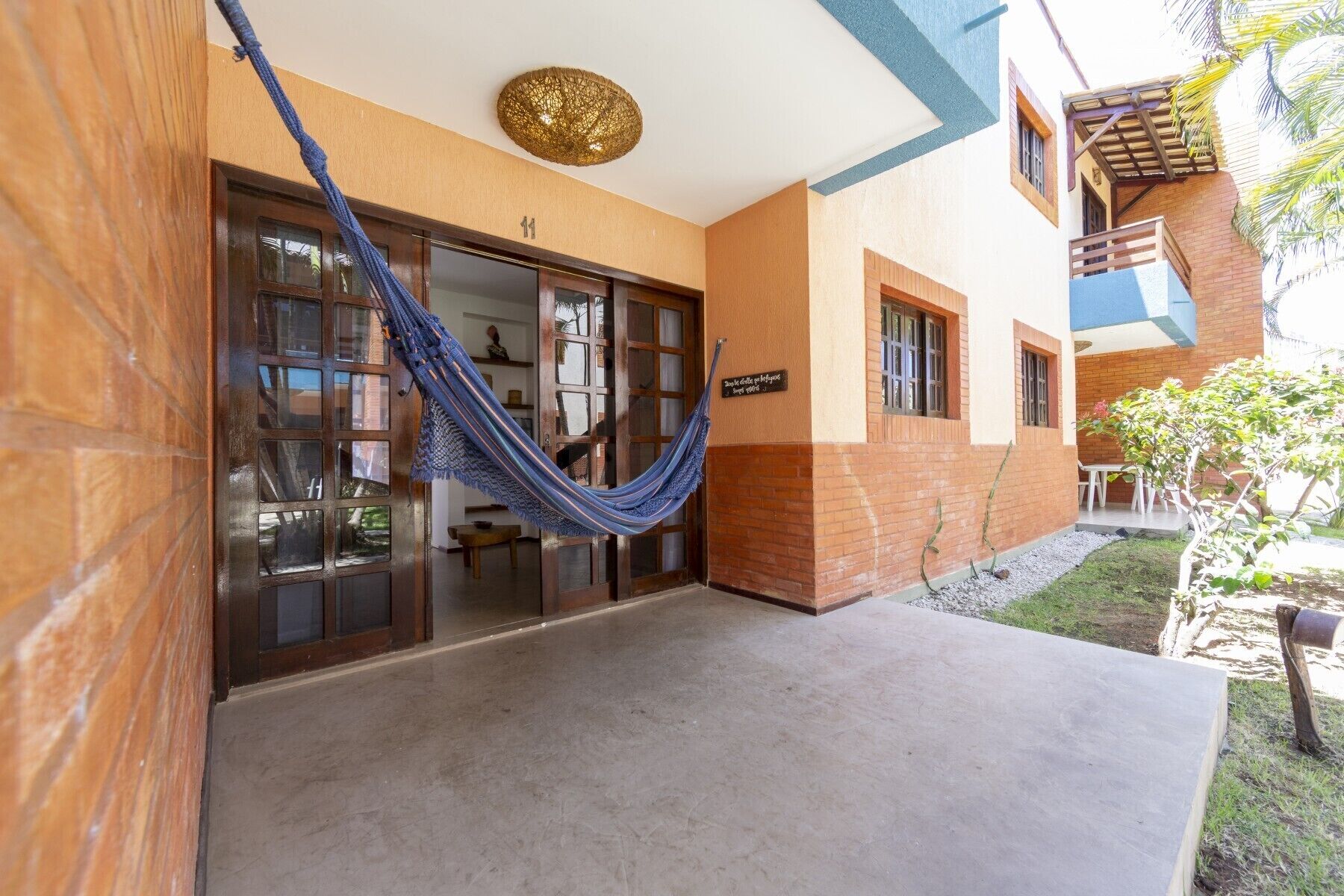 A building entrance with a blue hammock, a sign reading "Hotel de la Playa", and a small outdoor seating area with tables and chairs.