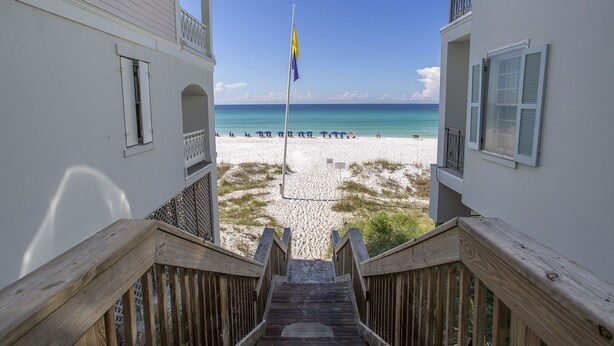 A wooden staircase leading to a beach with a flagpole and umbrellas. - Bella Mar - Villas of Frangista, Community Pool, Walk to the Beach + Dining! (Miramar Beach)