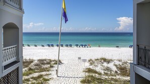 A beach view with a flagpole, beach umbrellas, and a clear blue sky. - Bella Mar - Villas of Frangista, Community Pool, Walk to the Beach + Dining! (Miramar Beach)