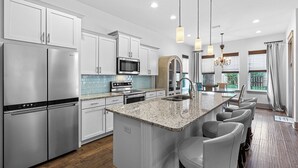 A modern kitchen with stainless steel appliances, a granite countertop, and a bar area with seating. - Bella Mar - Villas of Frangista, Community Pool, Walk to the Beach + Dining! (Miramar Beach)