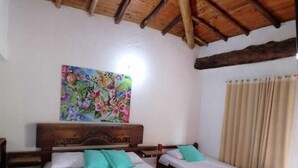 Une pièce avec un plafond en bois, un lit avec une tête de lit, deux tables de chevet, un tableau au mur et une fenêtre avec des rideaux.