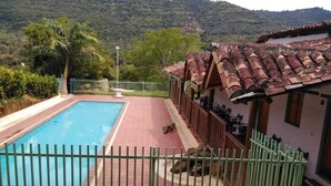 Une piscine dotée d’une terrasse carrelée, d’une zone délimitée par une clôture et d’un bâtiment surmonté d’un toit en tuiles.