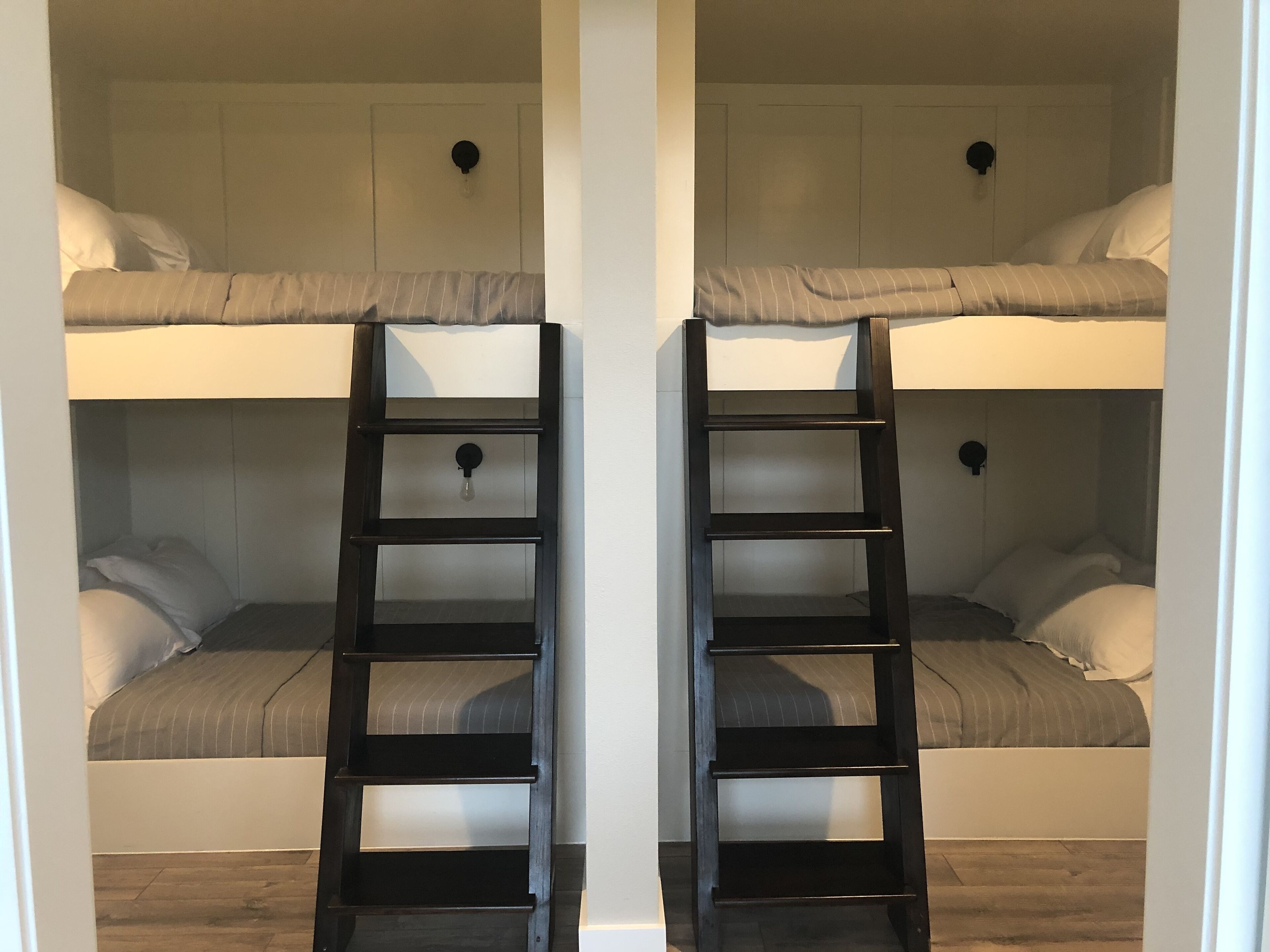 A bunk bed room with two black ladders, white walls, and wooden flooring.