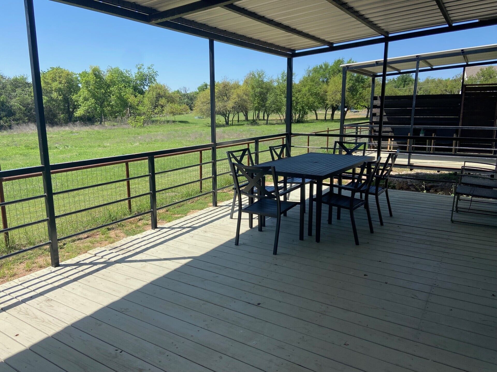 Un patio al aire libre con una mesa y sillas, rodeado por una barandilla de metal, con vistas a un campo cubierto de césped.